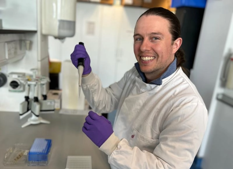 Dr Dylan Ryan, wearing a lab coat, pipettes chemicals in a laboratory.