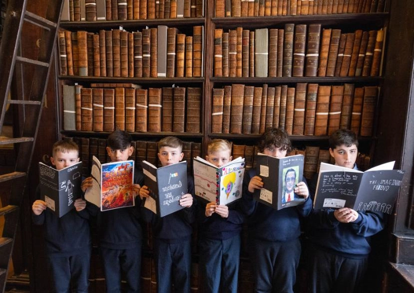 Group of 6 boys holding books against backdrop of bookshelves