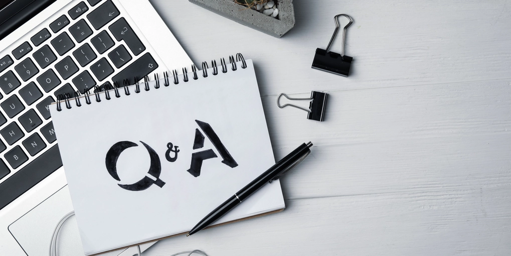 A laptop on a desk with a notebook on top with Q&A written in it