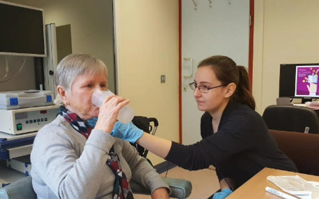 Lady having a sip of water while a health professional helps
