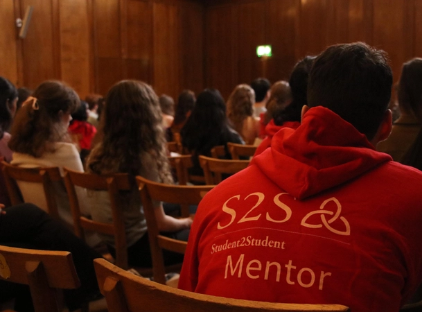 An S2S volunteer wearing a red hoodie with white letters on the back, which reads &ldquo;S2S Student2student Mentor&rdquo;. 