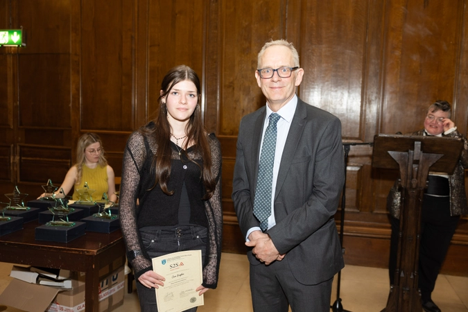 student in black dress holding cert paper beside man in suit