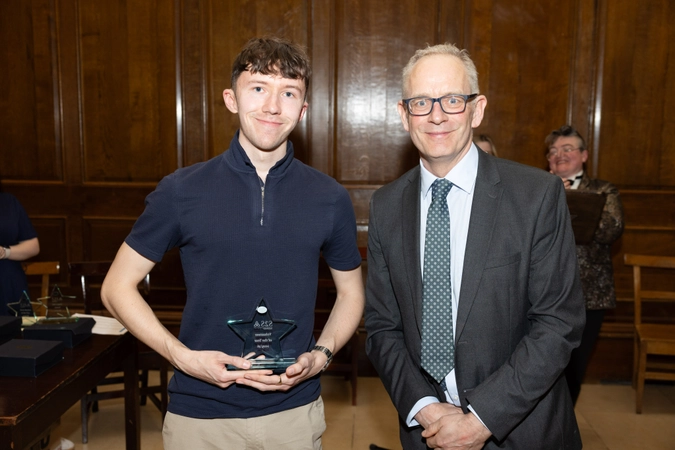 man wearing polo holding a crystal star trophy standing beside man in suit wearing glasses and tie