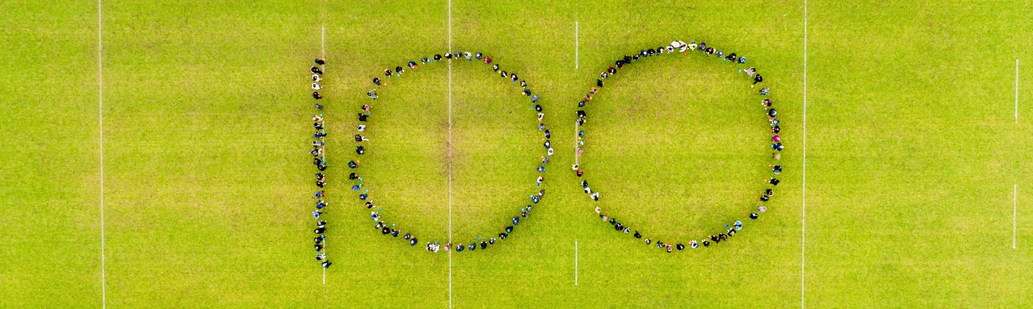A group of people on the rugby pitch forming a shape of 100