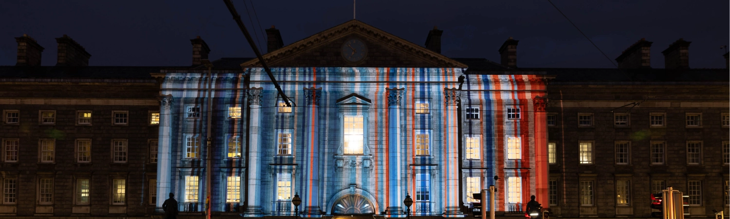 An image of Trinity's Front Gate with a projection of Dublin's Climate Stripes, designed by Professor Ed Hawkins
