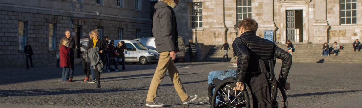 A wheelchair user moves across and accessible pavement at Parliament Square Trinity College Dublin