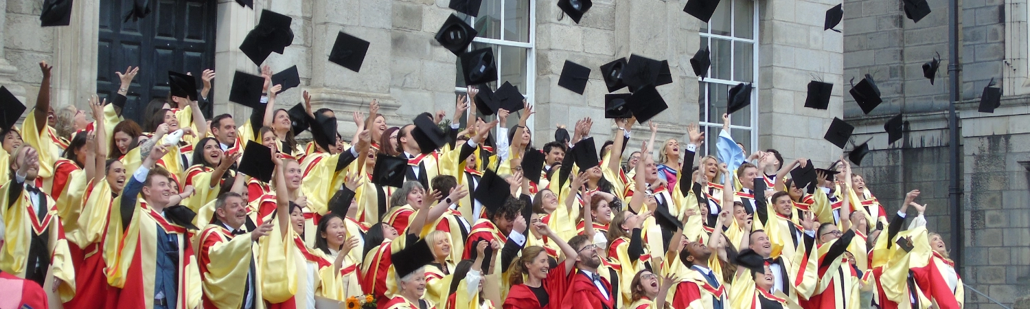 Literary Translation students on graduation day wearing robes and throwing their caps in the air.