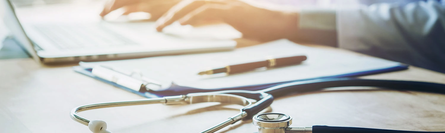 Doctor typing information on Laptop in Hospital office focus on Stethoscope