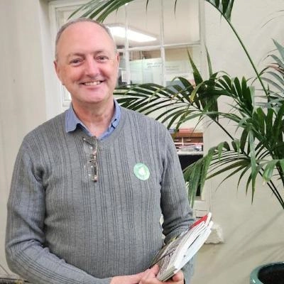 Marcus smiling holding flyers and standing next to tropical plant