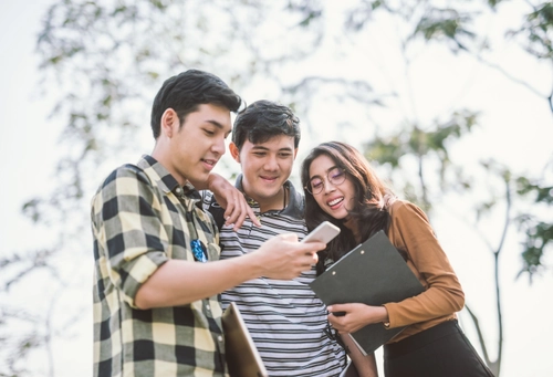 Three students looking at someone's phone outside