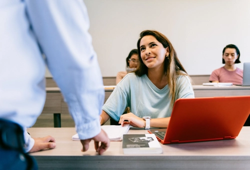Student sitting at the front of a lecture hall with professor's back to camera