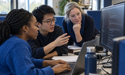 3 individuals engaging around a computer coding