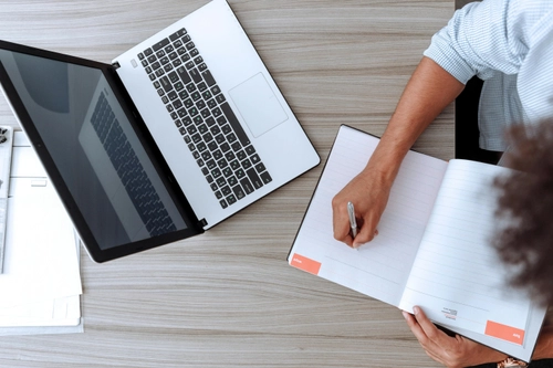 Person working on laptop with a notepad