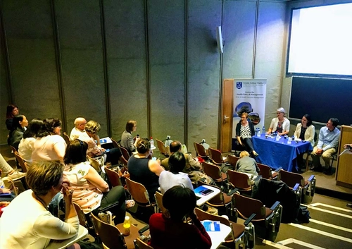 Panel of lecturers at table delivering lecture to audience in tiered theatre