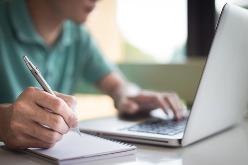 Student working at laptop, taking notes.