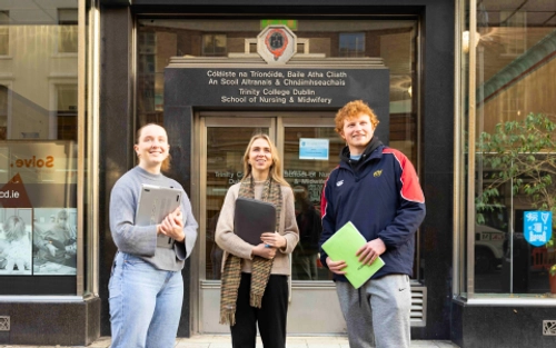 Three students stand outside the School of Nursing & Midwifery building