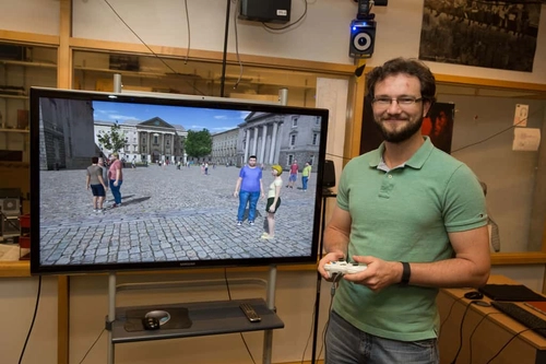 A degree student standing beside a TV screen showing a CGI presentation