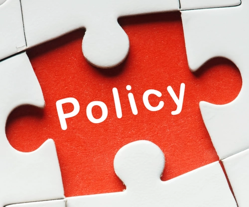 A white jigsaw missing a piece. The missing piece area is read and has Policy written on it