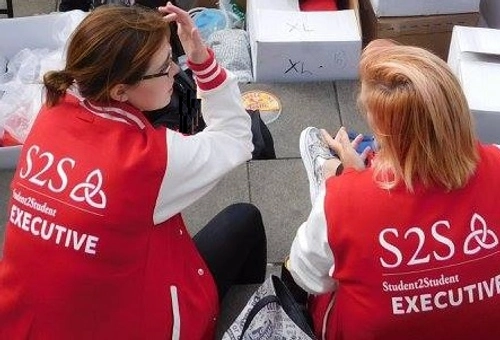 Two students sitting with their back to the camera. They are wearing red and white varsity jackets that say S2S executive on the back.