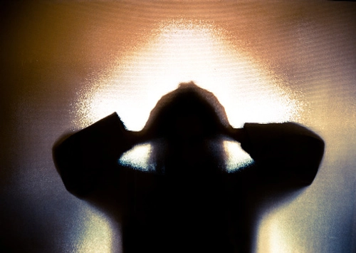shadowy figure holding hands to head