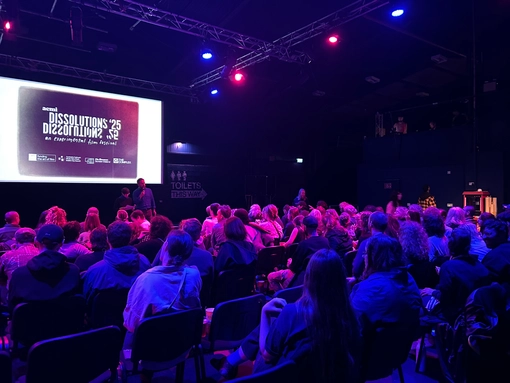 A dark theatre full of people with slides on the screen