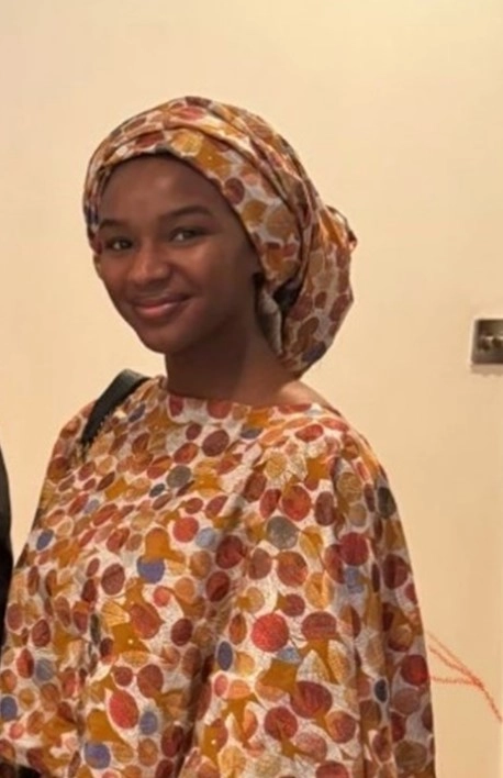 Maryam Yabo, Ph.D Researcher standing against an orange background