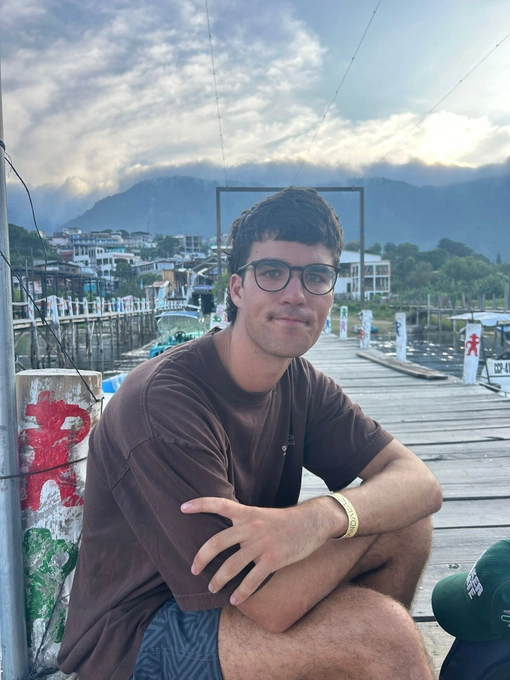 Man with Short dark hair, wearing glasses. They are sitting outside.