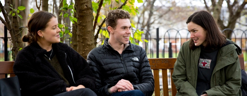 Three students sit on a bench
