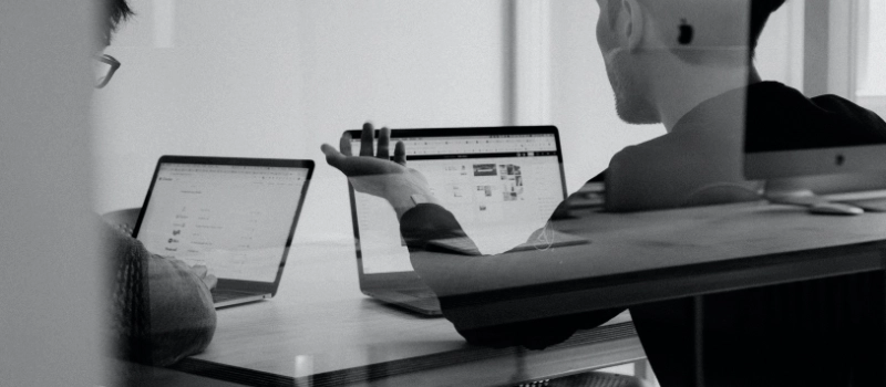 Image of two people sitting by laptops appearing to work together