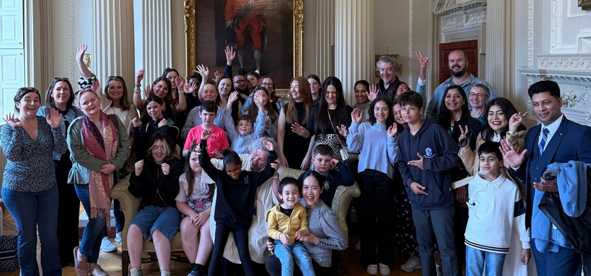 Large group photo of Linda, students, and their children taken in the Saloon of the Provost's House. Some people are cheering for the camera.