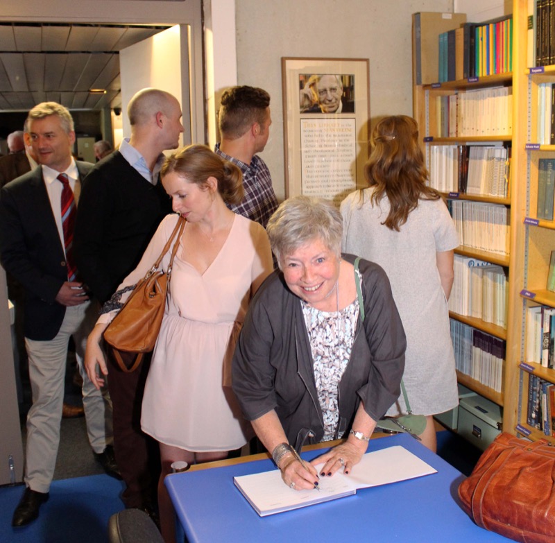 At the Freyne Library launch: Dr Gail Grossman Freyne signing the Visitors' Book, with daughters Sarah and Bridget and their husbands looking at the Storyboard and photo of Prof Seán Freyne