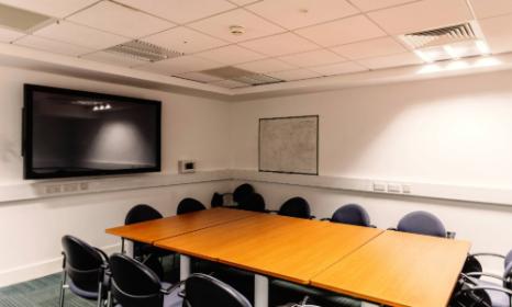Rom b1.06. This room has a large conference table with chairs in it and a large screen on the wall