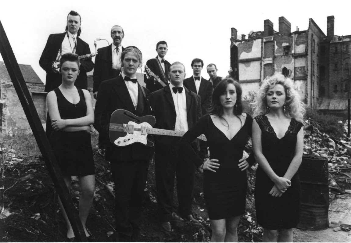 Black and white photo of cast of The Commitments film - a screenshot of the scene where the characters gather as a band for marketing photos with a derelict building in the background.