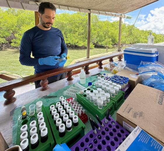 Researcher reviewing samples in the field on a boat, table full of tubes and samples.