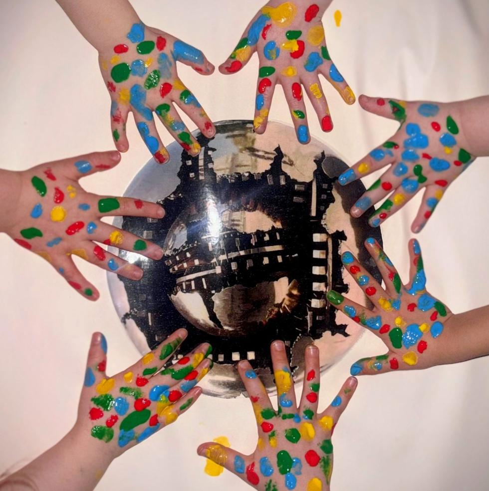 children's hands daubed with colourful paint, framing the Pomodoro sculpture