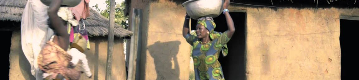 African village standing outside hut with basket on head