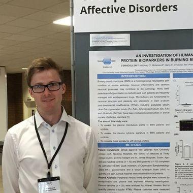 An image of physiology student David O’Driscoll standing in front of his project poster
