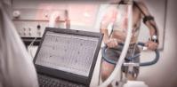 A close up photo of a computer monitoring a person's CO2 levels. The person can be seen in the adjacent room exercising on a bike