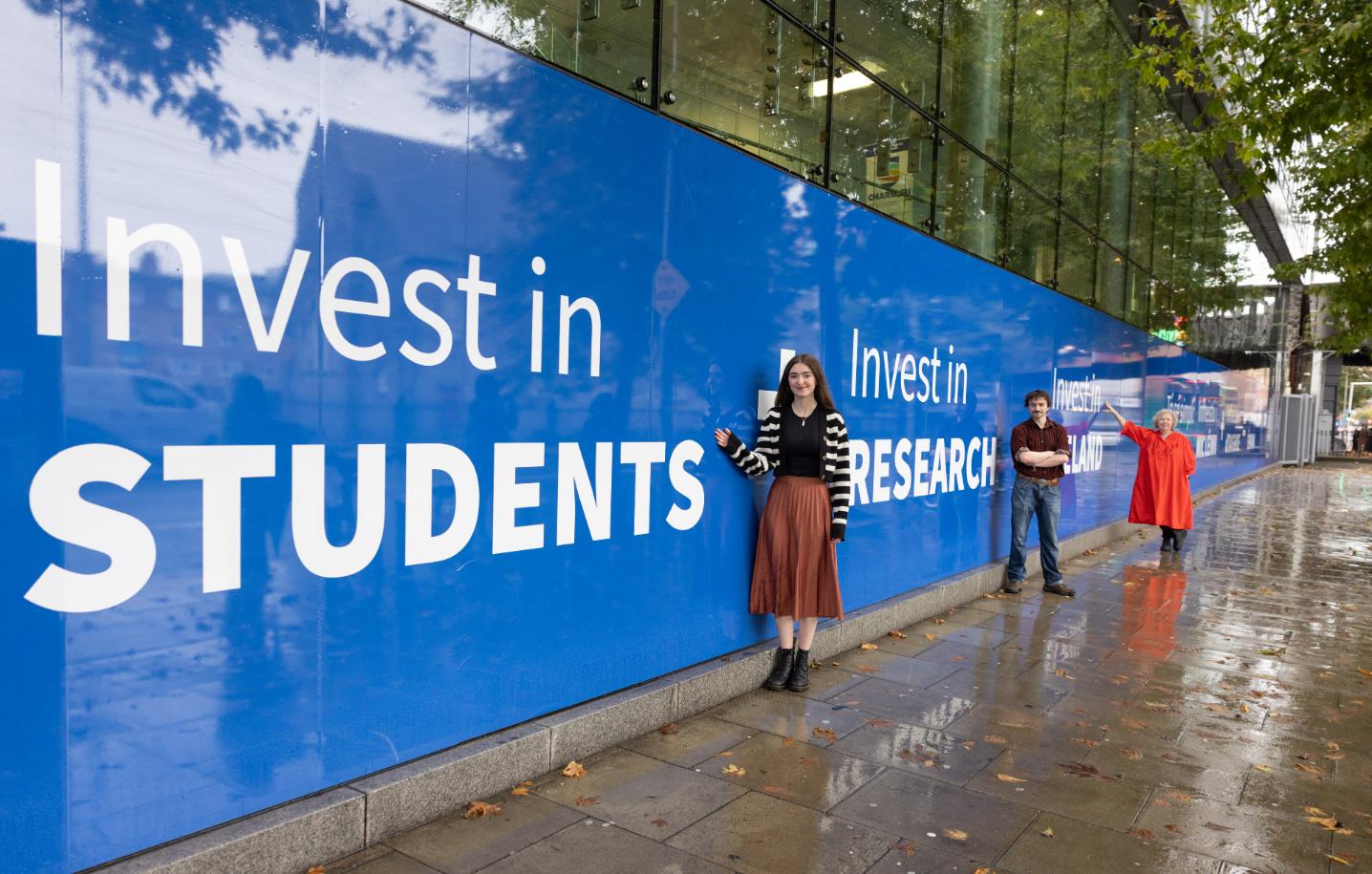 Three people stand in front of a large blue window installation