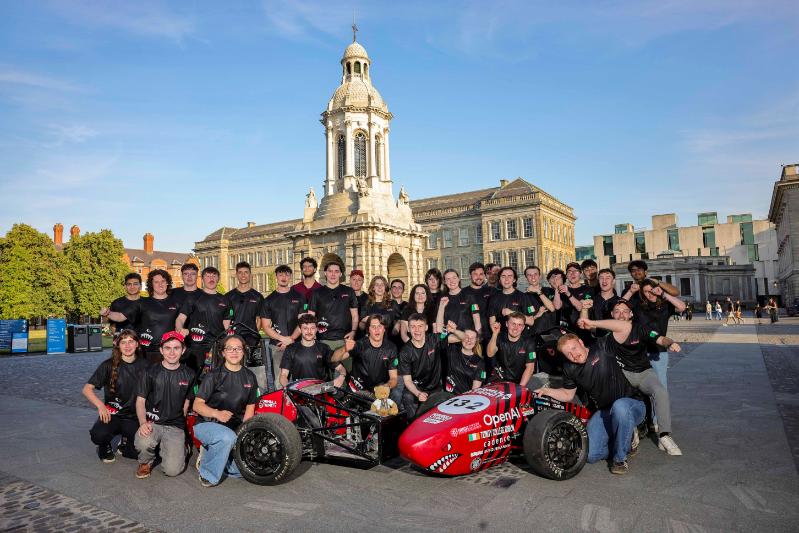 Many of the Formula Trinity student team with their formula race car, Bruce, in Front Square with the campanile behind.