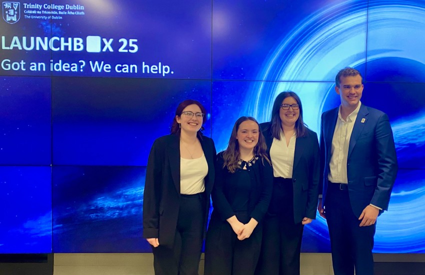 Three young women and a man pose in front of a blue screen