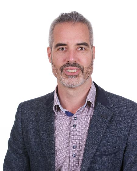 Professor Kevin Mitchell, wearing a dark suit jacket and smart shirt, smiling at the camera