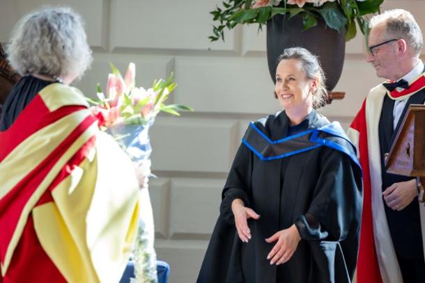 Provost Linda Doyle hands a bouquet of flowers to Lorraine Norton in the Exam Hall