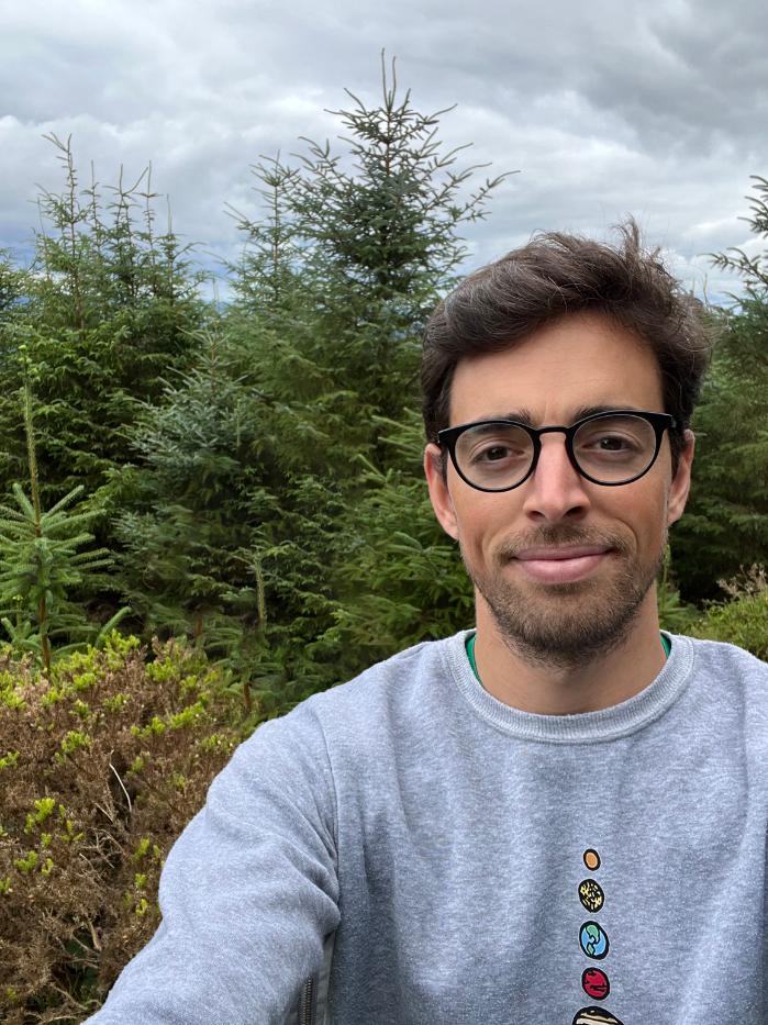 Prof. Luca Matra wearing glasses and a grey sweatshirt, with trees in the background
