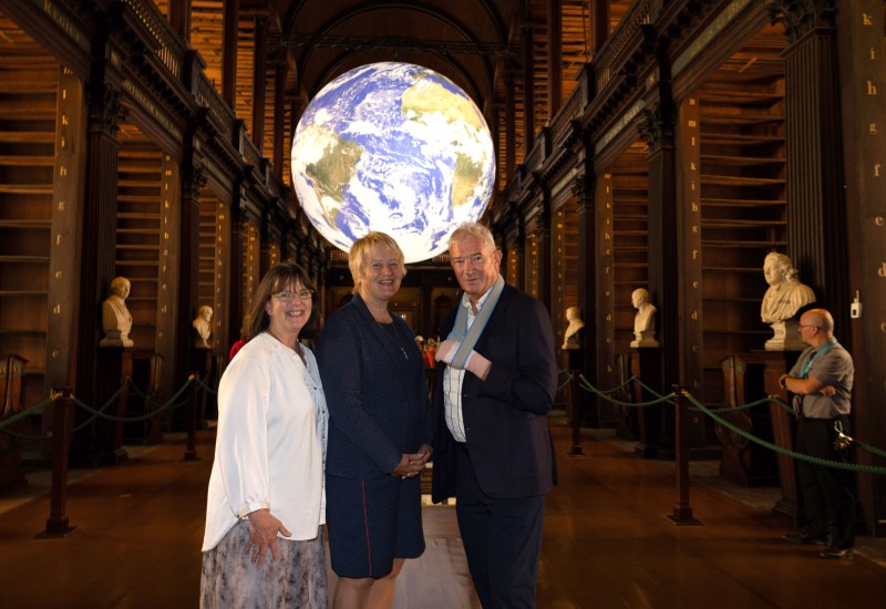 Two women and a man poses before an exhibit of a globe