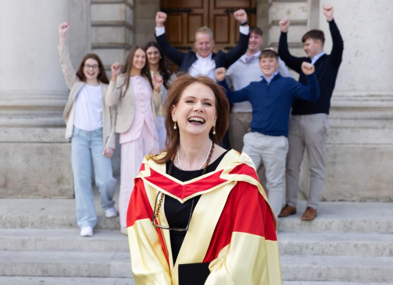 Rose Doolan-Maher, in graduation gown, smiles in Front Square after receiving her PhD. Her husband and six children look on.