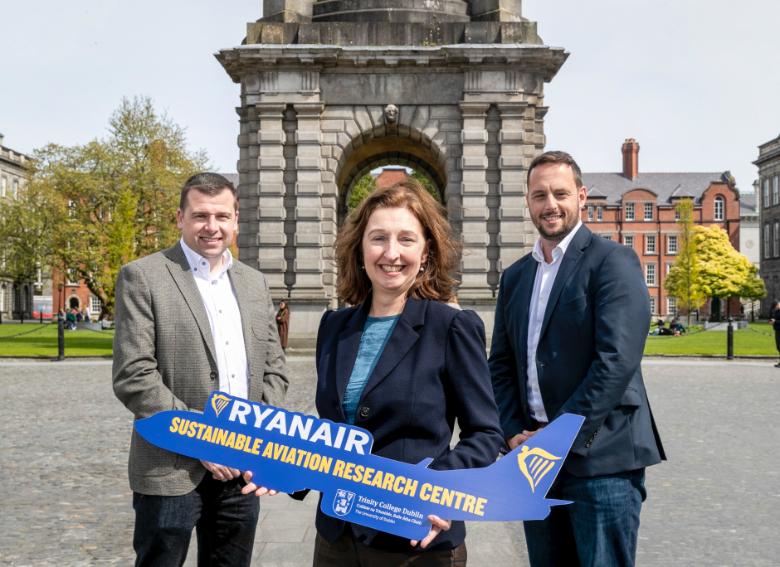 Thomas Fowler, Director of Sustainability and Finance, Ryanair; Prof. Sinéad Ryan, Dean of Research, Trinity; Steven Fitzgerald, Deputy Director of Sustainability and Finance, Ryanair. Model Ryanair planes are being held as the three people stand in front of Trinity's campanile in Front Square.