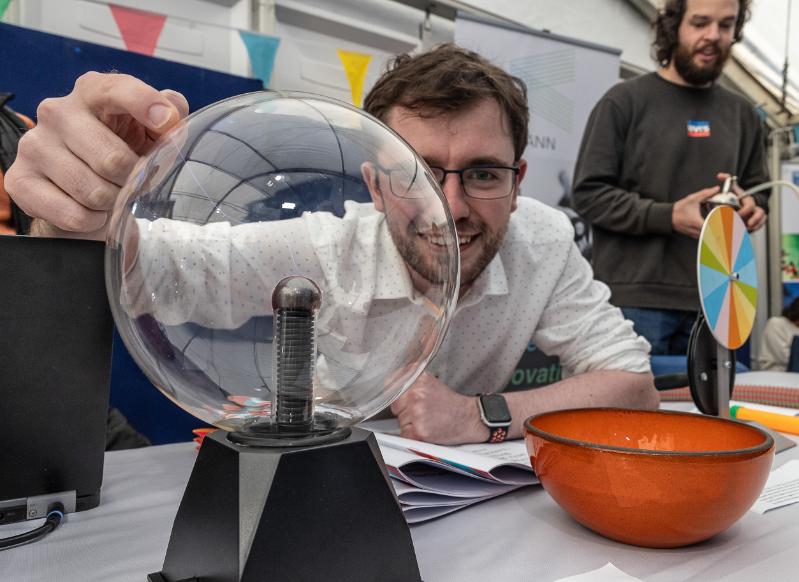 A man in a white lab coat looks through a prism with a bolt of electricity.