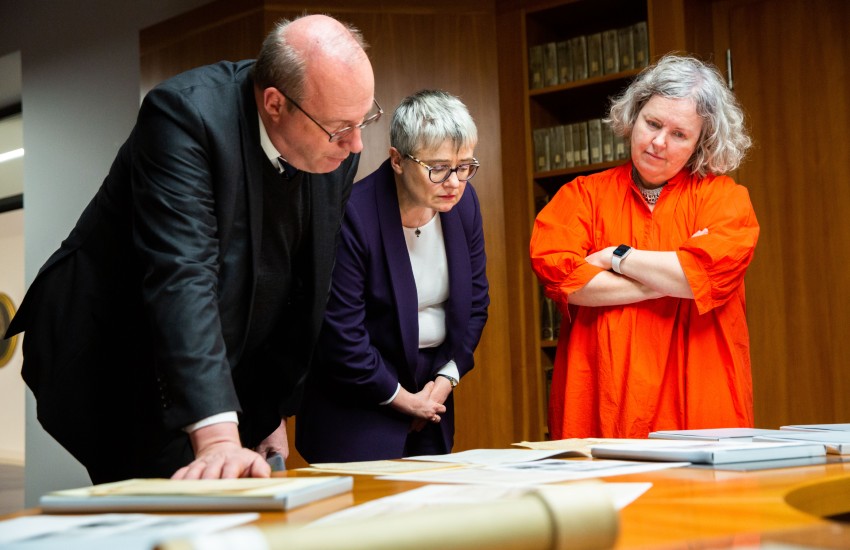 Three people examine a manuscript