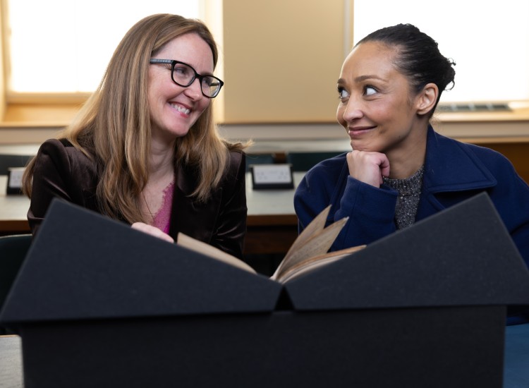 Two women smile as theye examine a manuscript